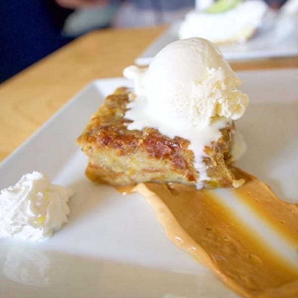 Bread pudding with vanilla ice cream, caramel, and whipped cream on a white plate.
