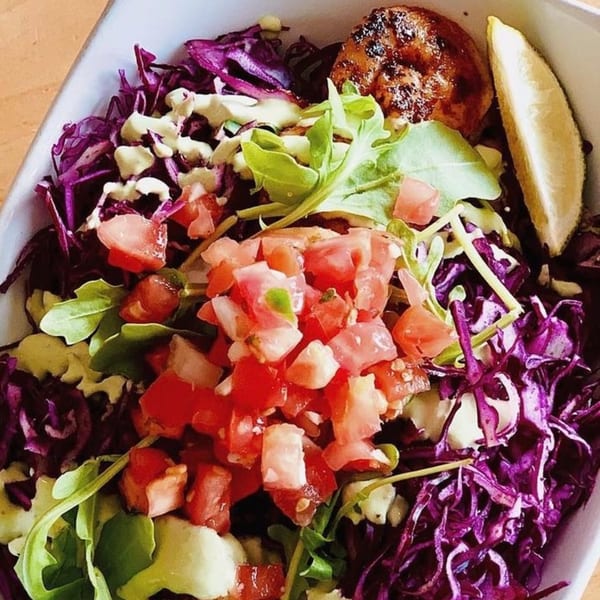 Fat Fish Taco's colorful bowl with purple cabbage, diced tomatoes, greens, grilled fish, and lime.