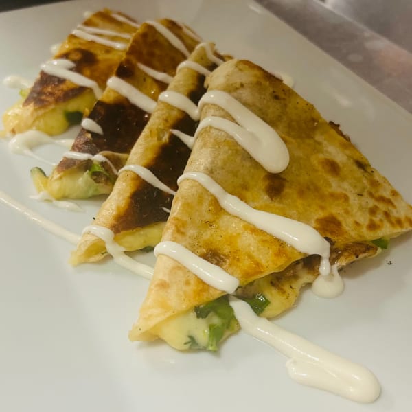 Four quesadilla wedges drizzled with white cream sauce, showcasing melted cheese and green peppers.