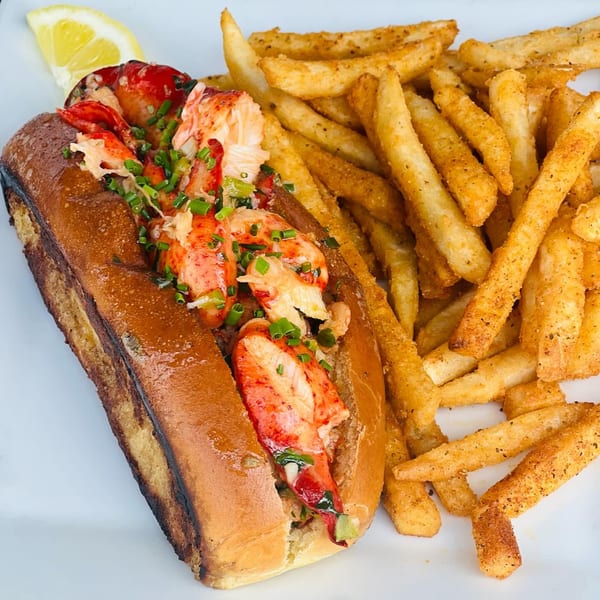 Fat Fish Taco's lobster roll with chives, served with a side of seasoned fries and a lemon wedge.